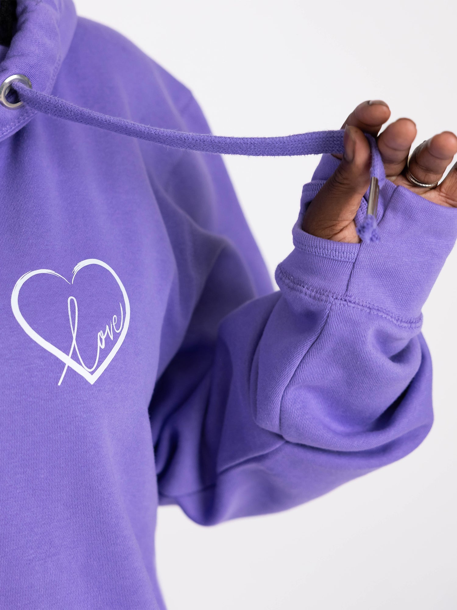 Close up to lavender purple womens cowl neck hoodie with Love heart. Cotton Polyester blend relaxed fit unisex oversized style hoodie design has love heart. White heart to upper left of the chest with word Love in white script font nestled within the heart. Long sleeves and Thumb loops to cuffs. Thick fabric drawstrings
