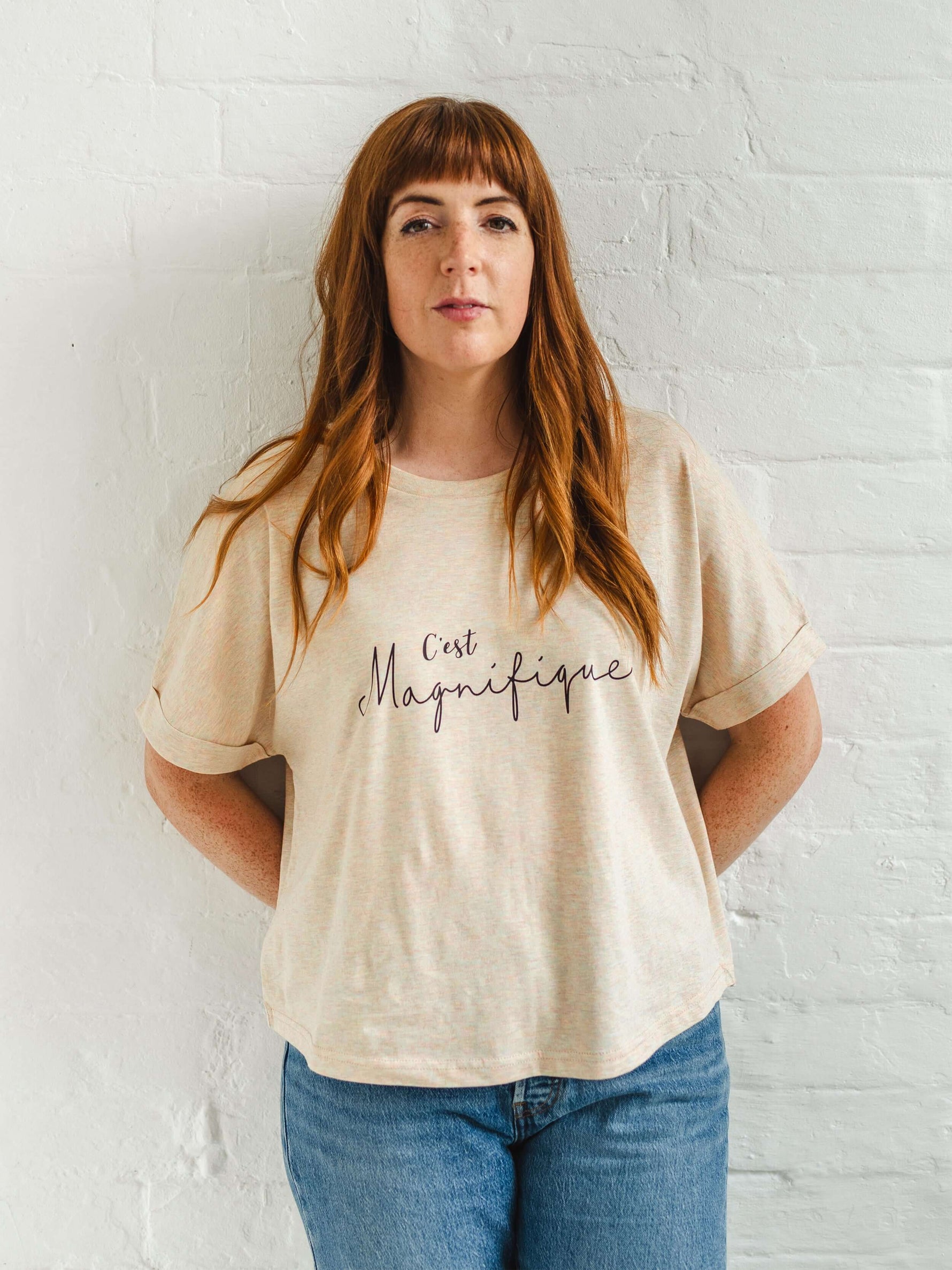 Ladies T-Shirt with dolman sleeve, rib neck collar and sleeve cuff fold. Rainbow Heather - light beige/cream base colour with multicolour flecks. Oversized women’s t-shirt with a short sleeves, inspired by the 1990s oversize trend.. Black slogan script font design reads French phrase C'est Magnifique