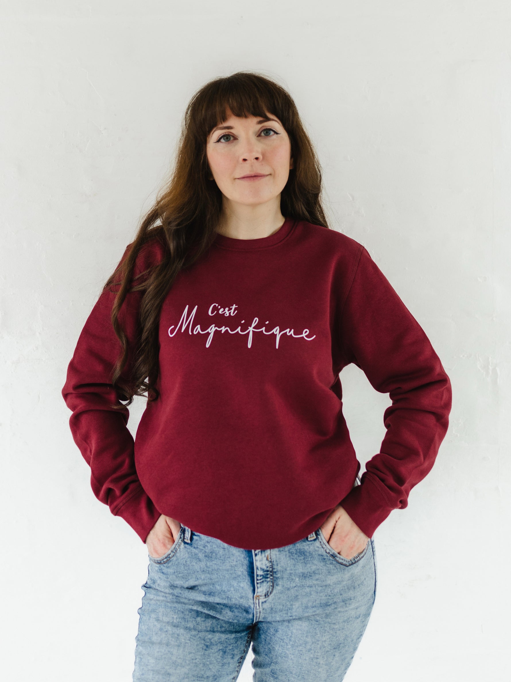Caucasian woman with long brown hair wearing blue acid wash jeans and a burgundy red relaxed fit sweatshirt jumper with crew round neck and long sleeves with cuffs.