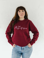 Caucasian woman with long brown hair wearing blue acid wash jeans and a burgundy red relaxed fit sweatshirt jumper with crew round neck and long sleeves with cuffs.