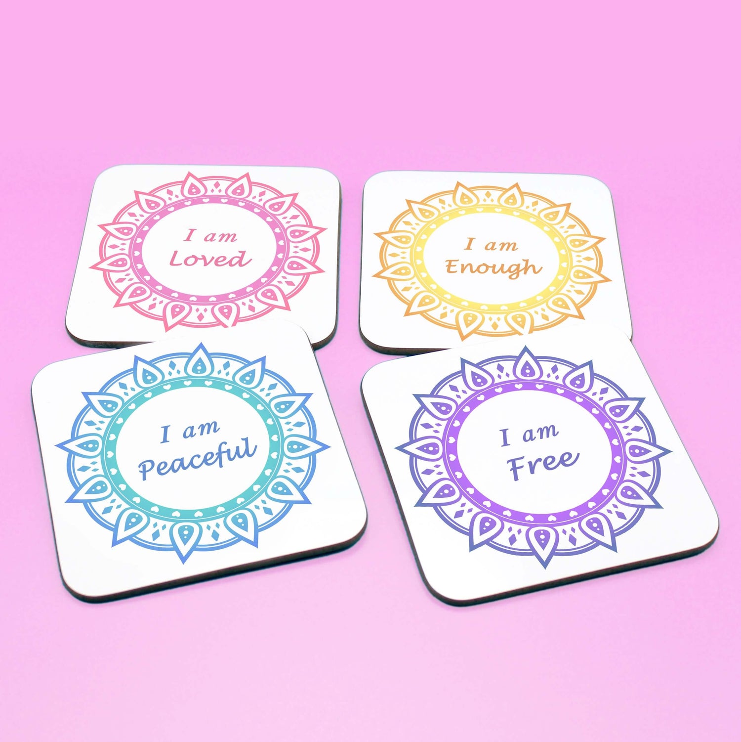 Wellbeing gift. Four square wooden backed personal affirmations coaster set. Theme is Letting Go in this set of four. Mandala design with daily affirmation wording inside the mandala. Affirmations read I am Loved (red and pink mandala), I am Enough (yellow and orange mandala), I am Peaceful (blue mandala), I am Free (Purple mandala)