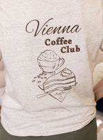 Close up of off white womens t-shirt with brown heather flecks with ' Vienna Coffee Club ' graphic design featuring a cup of coffee and cake. Ladies summer organic cotton t-shirt with shot sleeves