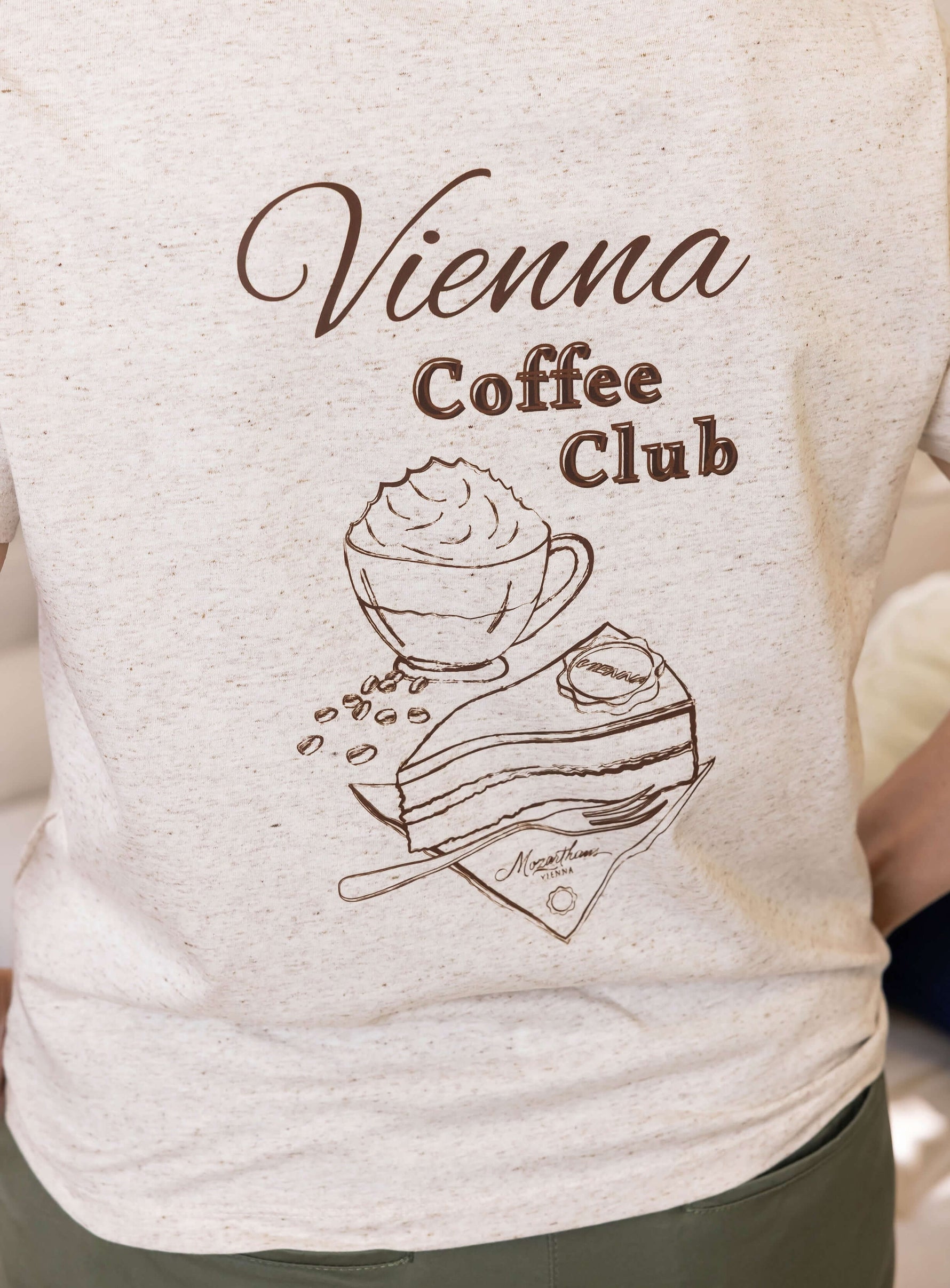 Close up of off white womens t-shirt with brown heather flecks with ' Vienna Coffee Club ' graphic design featuring a cup of coffee and cake. Ladies summer organic cotton t-shirt with shot sleeves
