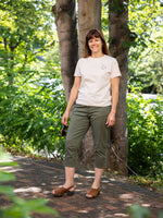 Woman standing outdoors with trees and greenery. Wears a ladies graphic tee off white with coffee cup small motif to chest. Short sleeve ladies t-shirt for summer. Coffee Club graphic on the back (not show in this image)