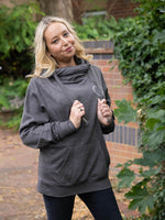 Model outdoors in nature wears womens Cowl Neck Hoodie - Dark Grey hoodie with silver metallic love heart motif. Charcoal ladies hoodie with Long sleeves and thumb loops to cuffs. Front kangaroo pouch pocket. Cross neck sweatshirt with hood