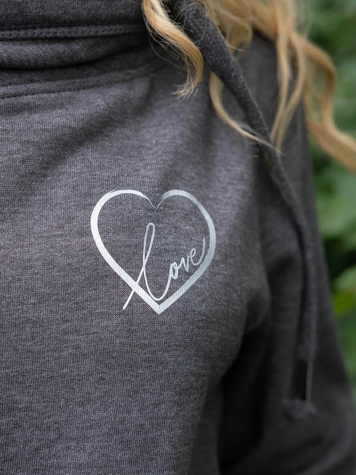 Close up of womens cowl neck hoodie in dark heather grey with silver love heart motif with word love in script inside heart outline graphic