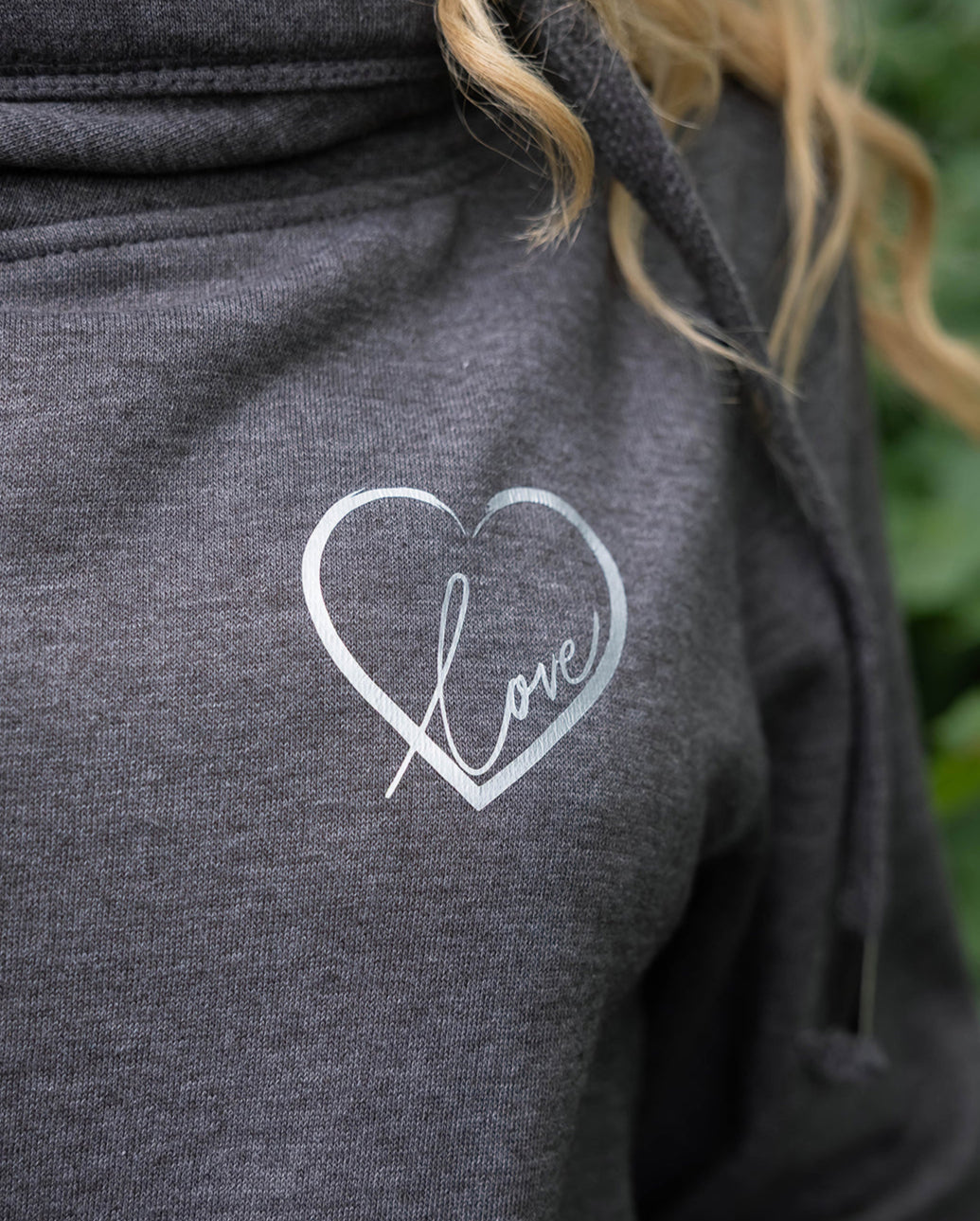 Close up of Womens Cowl Neck Hoodie - Dark Grey hoodie with silver metallic love heart motif. and words Love in script font inside heart. Cross neck hood and metallic eyelet for thick cotton drawstrings with metal toggle  