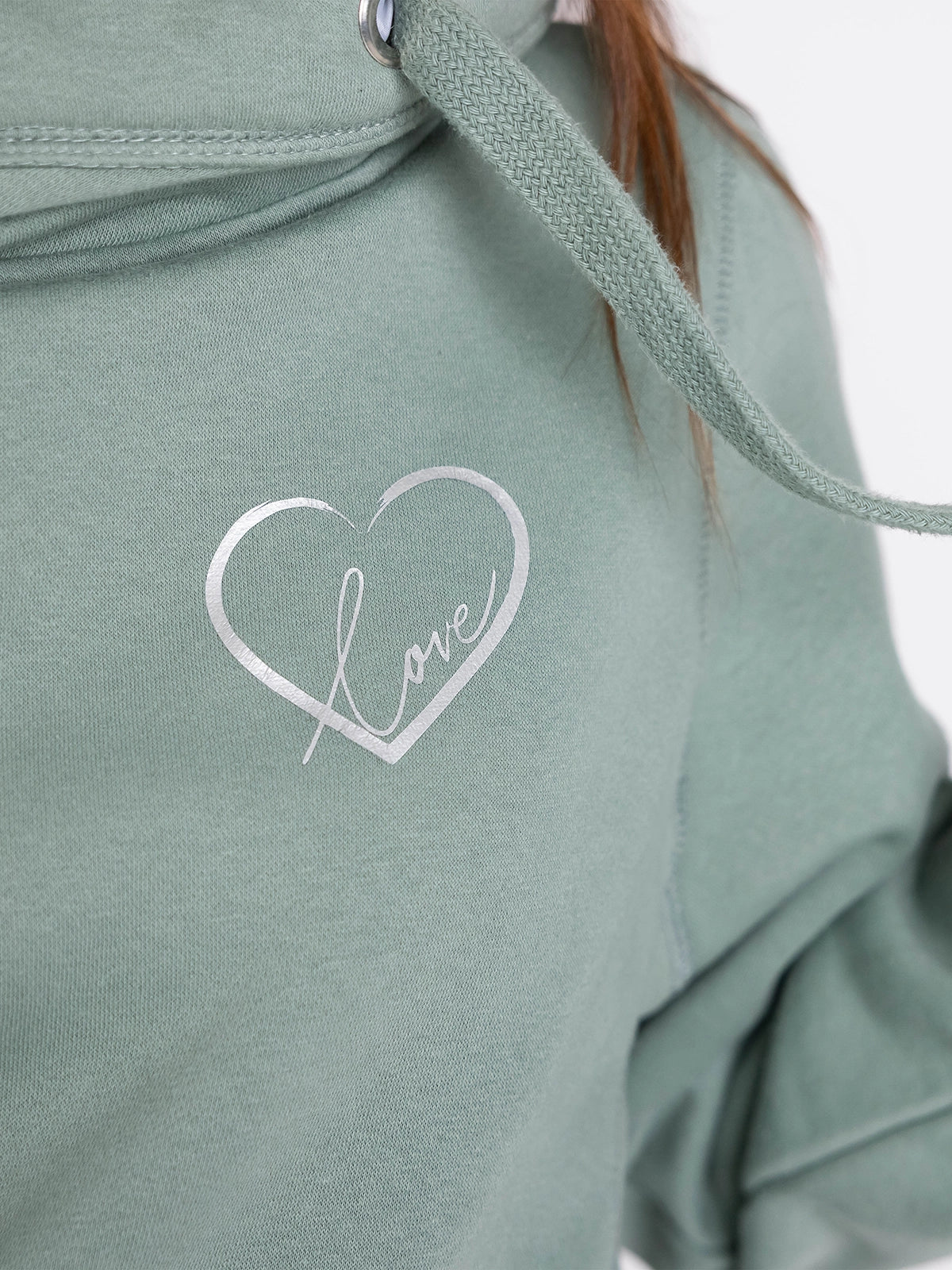 Womens Cowl Neck Hoodie - Close up of Dusty green hoodie with silver metallic love heart outline motif with the word love in silver script inside. Long sleeves Cross neck sweatshirt with hood and thick fabric drawstrings