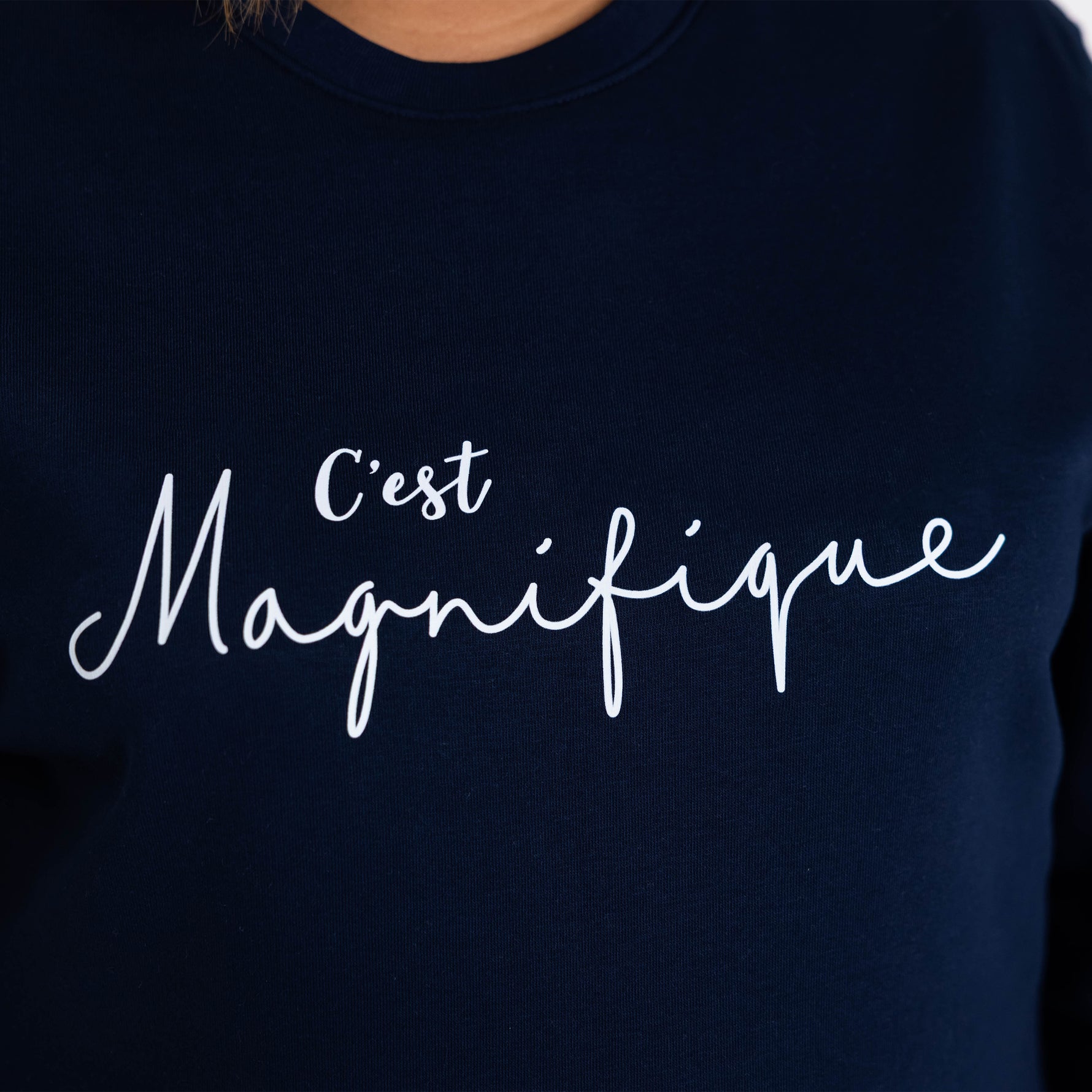 Close up of Womens navy blue relaxed fit french slogan sweatshirt jumper with crew round neck and long sleeves with cuffs. Ladies top with white script font reads C'est Magnifique