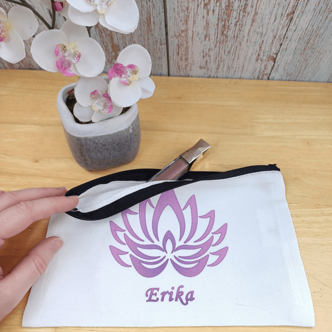 Gift for yoga lovers. Small personalised yoga theme make up bag. White with black zipped opening. Purple lotus flower design and name in purple below. Close up shows lip gloss stick half way out of opening to illustrate size capacity