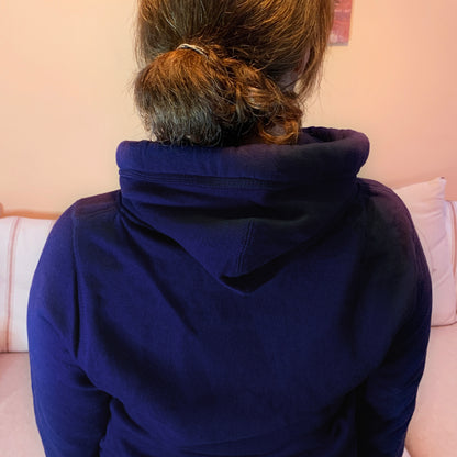 Back of a woman with brown hair tied up. wearing a navy blue unisex oversized hoodie photo shows upper torso to display hood design and long sleeves 