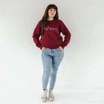 Full length photo of a caucasian woman in her 40s with long brown hair wearing light blue acid wash jeans and a burgundy red on trend ladies sweatshirt, oversized fit with crew neck and long sleeves.