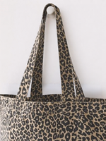 Close up of washed effect finish leopard print women's Canvas Shopper. Animal print tote bag is hanging on a round hook against a plain background