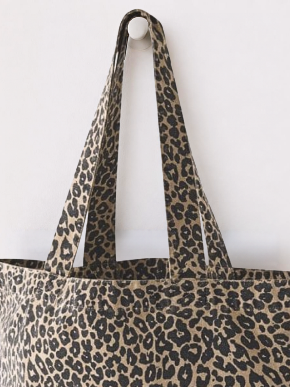 Close up of washed effect finish leopard print women's Canvas Shopper. Animal print tote bag is hanging on a round hook against a plain background
