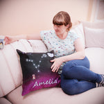 Woman sitting on a sofa with a cup of tea looking at a personalised cushion next to her with zodiac sign Virgo. Space backdrop black sky with stars fading to deep pink purple hue at bottom of the cusion. Personalised with girls name at the bottom, Small owl on a branch to the left of star sign constellation at centre and top right cute smiling moon and two stars. 18 inch faux suede home decor constellation cushion