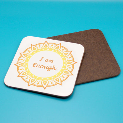 White personal affirmation coaster with yellow and orange mandala design. Daily affirmation reads I am Enough. Coaster underneath shows wood backing