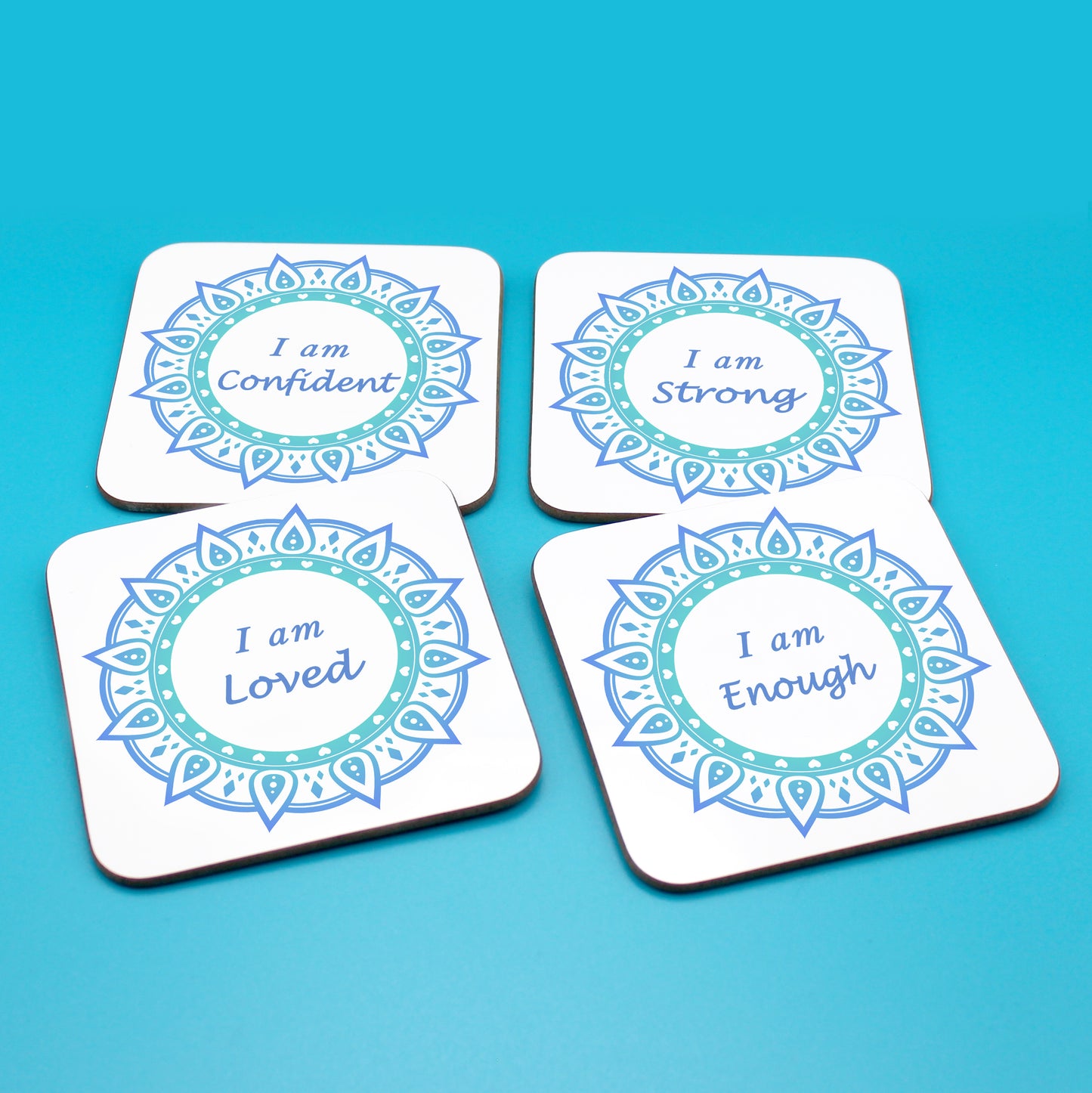 Wellbeing gift. Four square wooden backed positive affirmations coaster set. Mandala design with daily affirmation wording inside the mandala.  Each Affirmations coaster individually reads I am Loved, I am Enough, I am Confident, I am Strong (all mandalas are blue in this set)