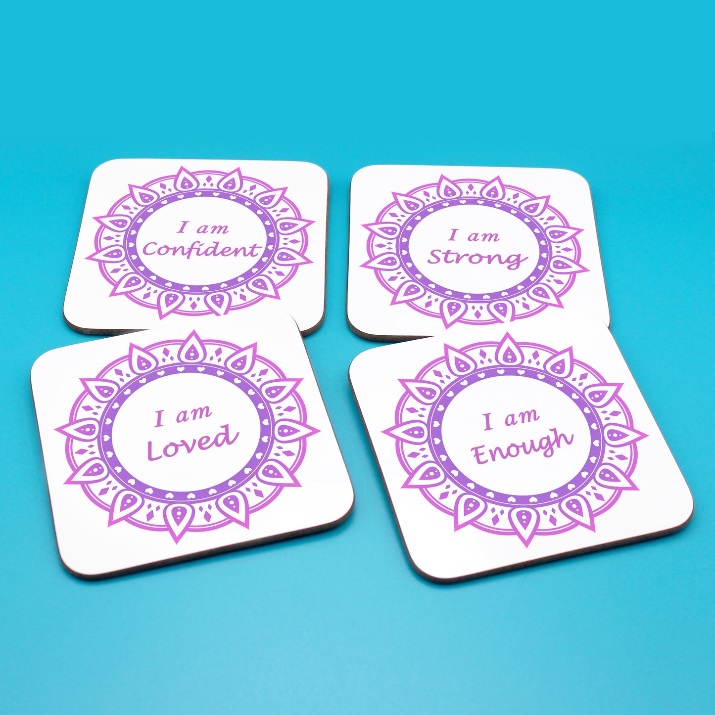 Wellbeing gift. Four square wooden backed positive affirmations coaster set. Mandala design with daily affirmation wording inside the mandala.  Each Affirmations coaster individually reads I am Loved, I am Enough, I am Confident, I am Strong (all mandalas are two tone purple  in this set)