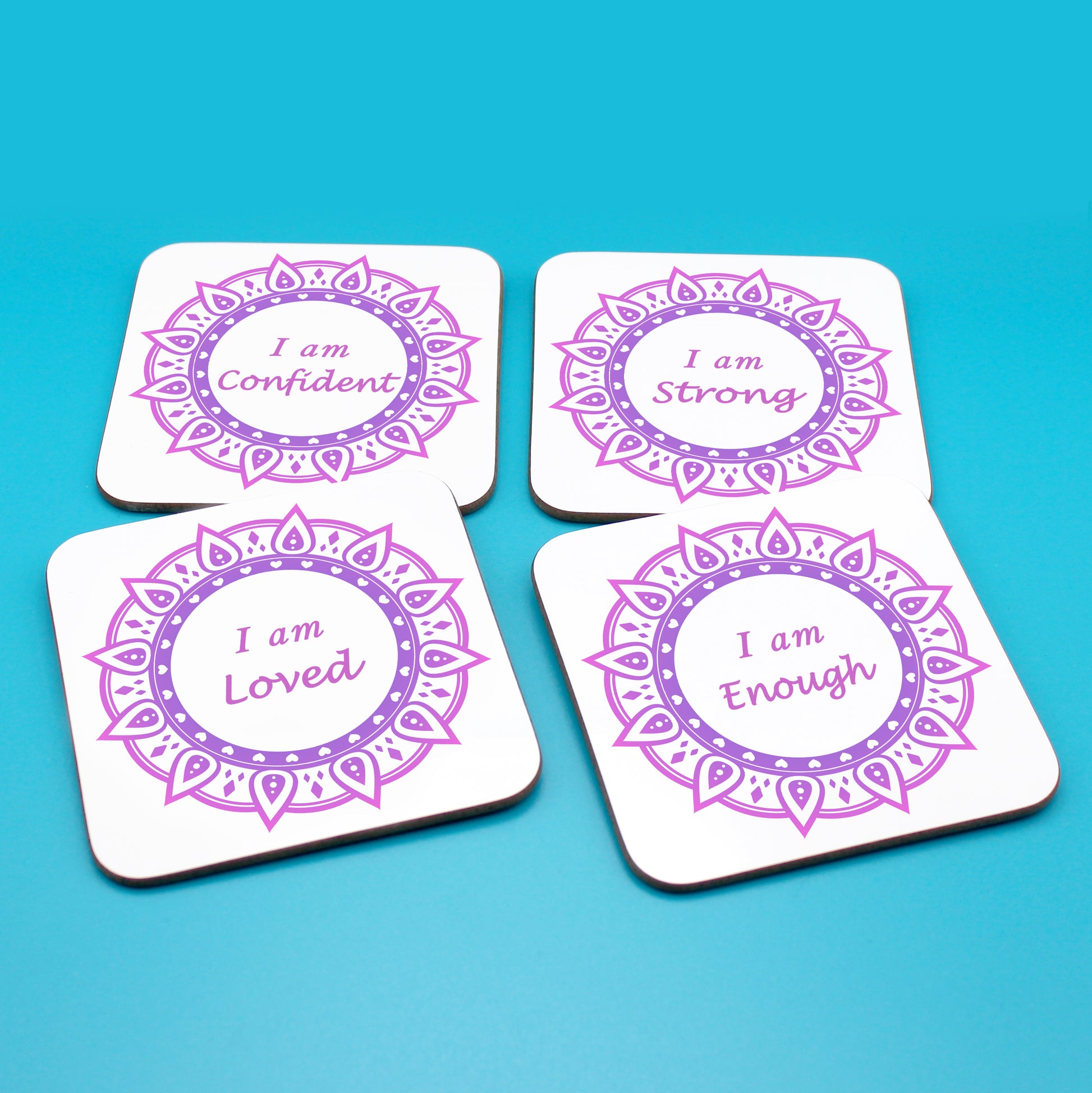 Wellbeing gift. Four square wooden backed positive affirmations coaster set. Mandala design with daily affirmation wording inside the mandala.  Each Affirmations coaster individually reads I am Loved, I am Enough, I am Confident, I am Strong (all mandalas are two tone purple  in this set)