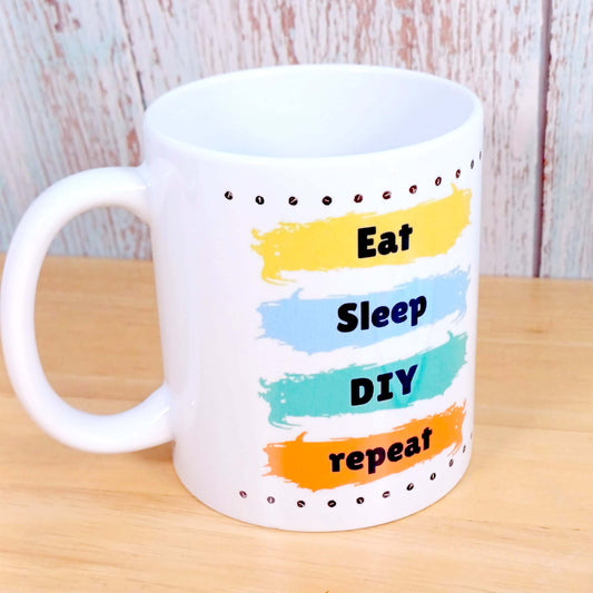 Gift for Dad or DIY enthusiast. White ceramic mug with line of screws top and bottom and 4 different colour paint stripes design. Each stripe of paint has a word in vertical sequence. Eat Sleep DIY repeat. Perfect Birthday or Father's Day gift idea