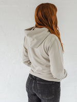 Woman with auburn long hair standing with her back turned to show hood  wears a Ladies coffee themed oversized fit hoodie. Stone grey hoodie top with coffee cup and saucer design. Black outline with steam from cup shaped into a heart. Writing above reads Coffee & Procrastination. Below reads Society FOUNDING MEMBER Est. 7am. Worn with black straight leg jeans