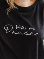 Close up of womens oversized black t shirt with short loose sleeves with roll cuffs. The ladies tshirt has the words Voulez Vous Danser in white