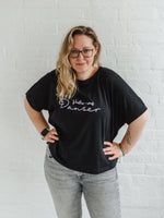 Woman wearing a black T-shirt with loose sleeves with roll cuffs worn with grey skinny jeans. The ladies tshirt has the words Voulez Vous Danser in white  Edit alt text