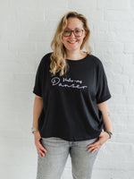 Woman wearing a black T-shirt with loose sleeves with roll cuffs worn with grey skinny jeans. The ladies tshirt has the words Voulez Vous Danser in white 