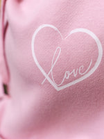 Close up to baby pink womens hoodie Love heart cross cowl neck casual fashion hoodie. Cotton Polyester blend relaxed fit unisex oversized style hoodie design has love heart. Whitert to upper left of the chest with word Love in white script font nestled within the heart.