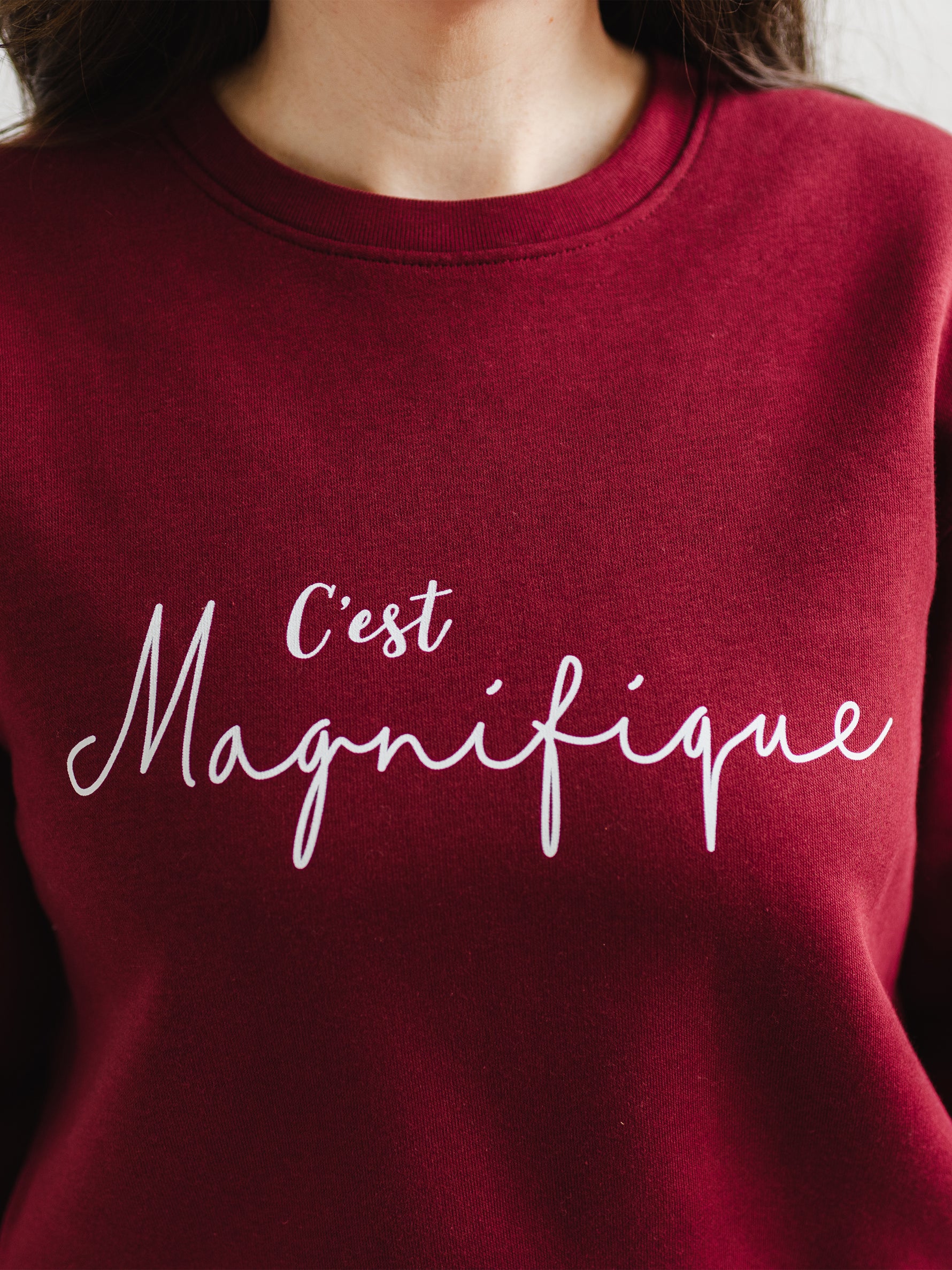 Ladies trendy sweatshirt with slogan french wording C'est Magnifique. Womens Burgundy red sweatshirt top with relaxed fit crew neck and long sleeves. Slogan is in white script font. 