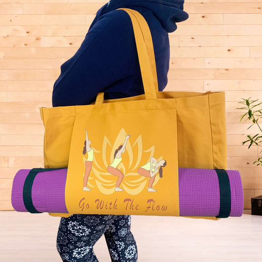 A woman in workout wear hoodie and leggings holding an amber coloured yoga bag on her shoulder in a fitness studio. The yoga mat bag hosts the words Go With The Flow and a graphic of a lotus flower and a light skinned woman in 3 yoga poses. A purple yoga mat is held by a pouch pocket on the front of the bag.