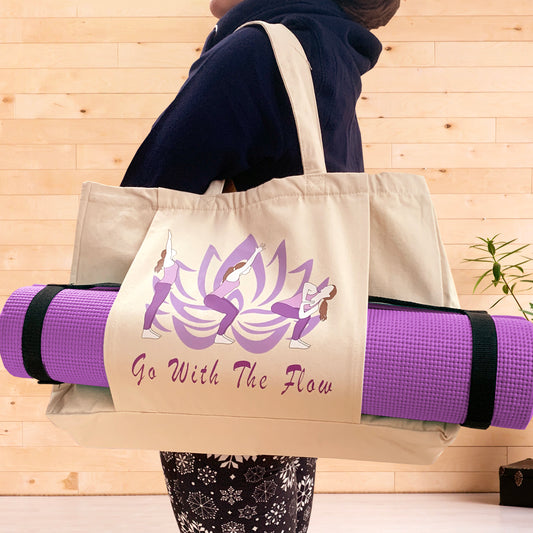 A relaxed woman holding a natural coloured yoga bag on her shoulder in a fitness studio. The bag hosts the words Go With The Flow and a graphic of a lotus flower and 3 yoga poses. A purple yoga mat is held by a pouch pocket on the front of the bag.