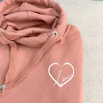 Close up to Dusty pink relaxed fit Love heart cross cowl neck casual fashion hoodie. Cotton Polyster blend relaxed fit unisex oversized hoodie design has love heart. White heart to upper left of the chest with word Love in white handwriting font nestled within the heart.