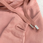 Close up to Dusty pink relaxed fit Love heart cross cowl neck casual fashion hoodie. Cotton Polyster blend relaxed fit unisex oversized hoodie design has love heart. White heart to upper left of the chest with word Love in white handwriting font nestled within the heart. Photo shows 4 hoodies with drawstrings metal toggles to ends and thumb holes to long sleeve arm cuffs