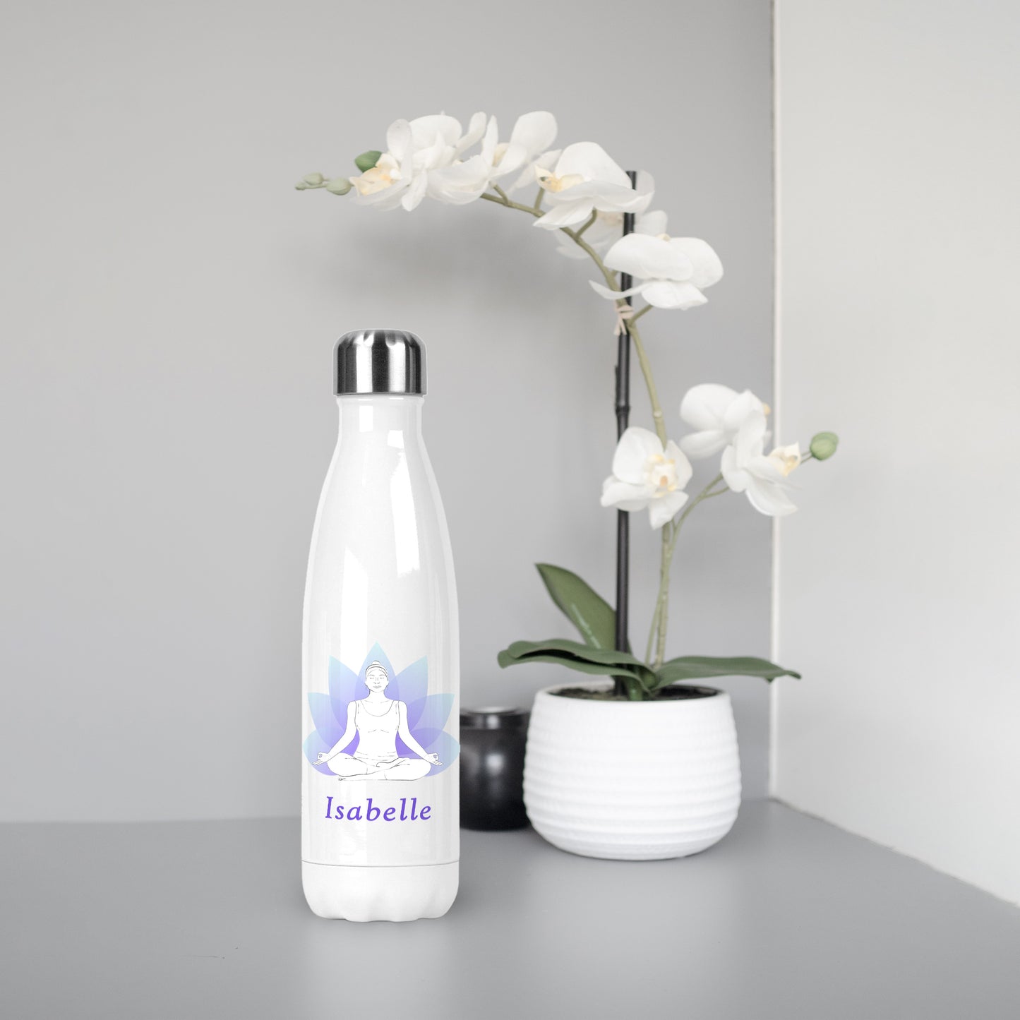 Personalised White 500ml reusable metal water bottle silver lid. Front design shown of two-tone blue and purple lotus flower. White outline woman in yoga meditation pose. Personalised purple font of name below. White orchid plant in background