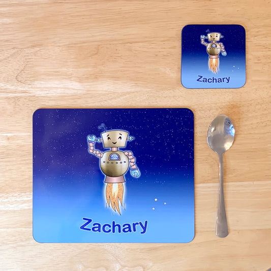 Blue star sky kids placemat set. Robot smiling with jets flying into space. Personalised with boy's name at the bottom of custom child's dinner mat and matching coaster. Tea spoon next to placemat