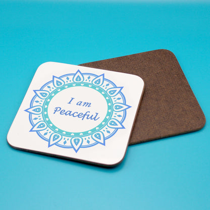 White personal affirmation coaster with blue mandala design. Daily affirmation reads I am Peaceful. Coaster underneath shows wood backing