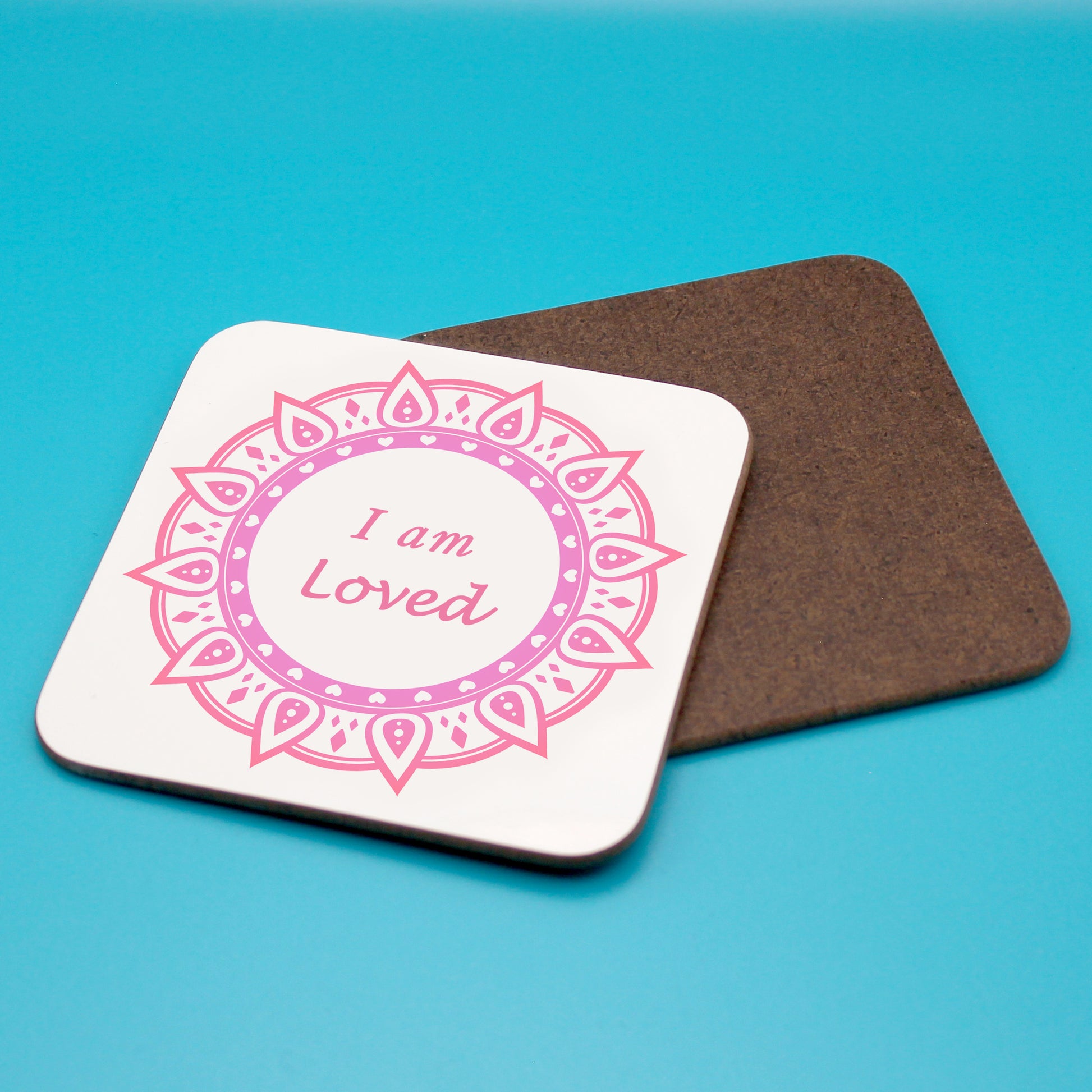 White personal affirmation coaster with pink and red mandala design. Daily affirmation reads I am Loved. Coaster underneath shows wood backing