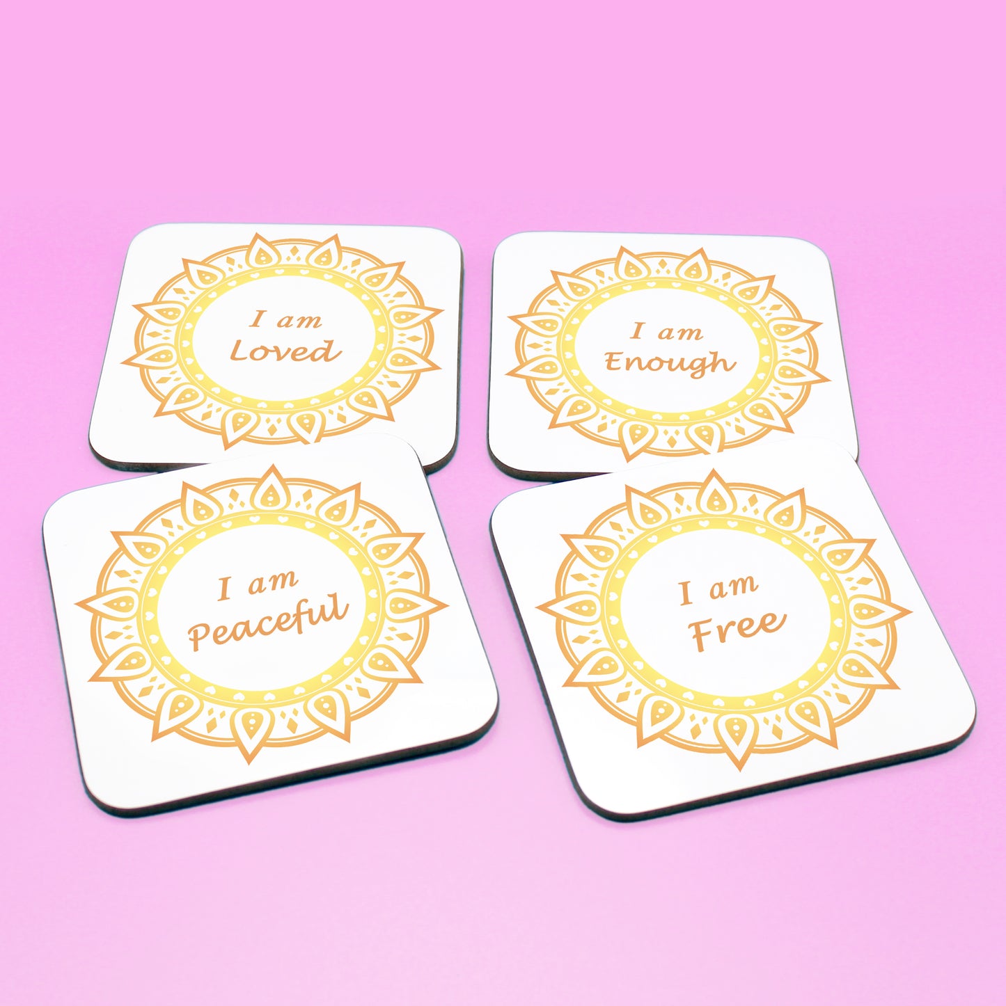 Wellbeing gift. Four square wooden backed personal affirmations coaster set. Theme is Letting Go in this set of four. Mandala design with daily affirmation wording inside the mandala.  Affirmations read I am Loved, I am Enough, I am Peaceful, I am Free (all coaster mandalas are a yellow and orange mandala),