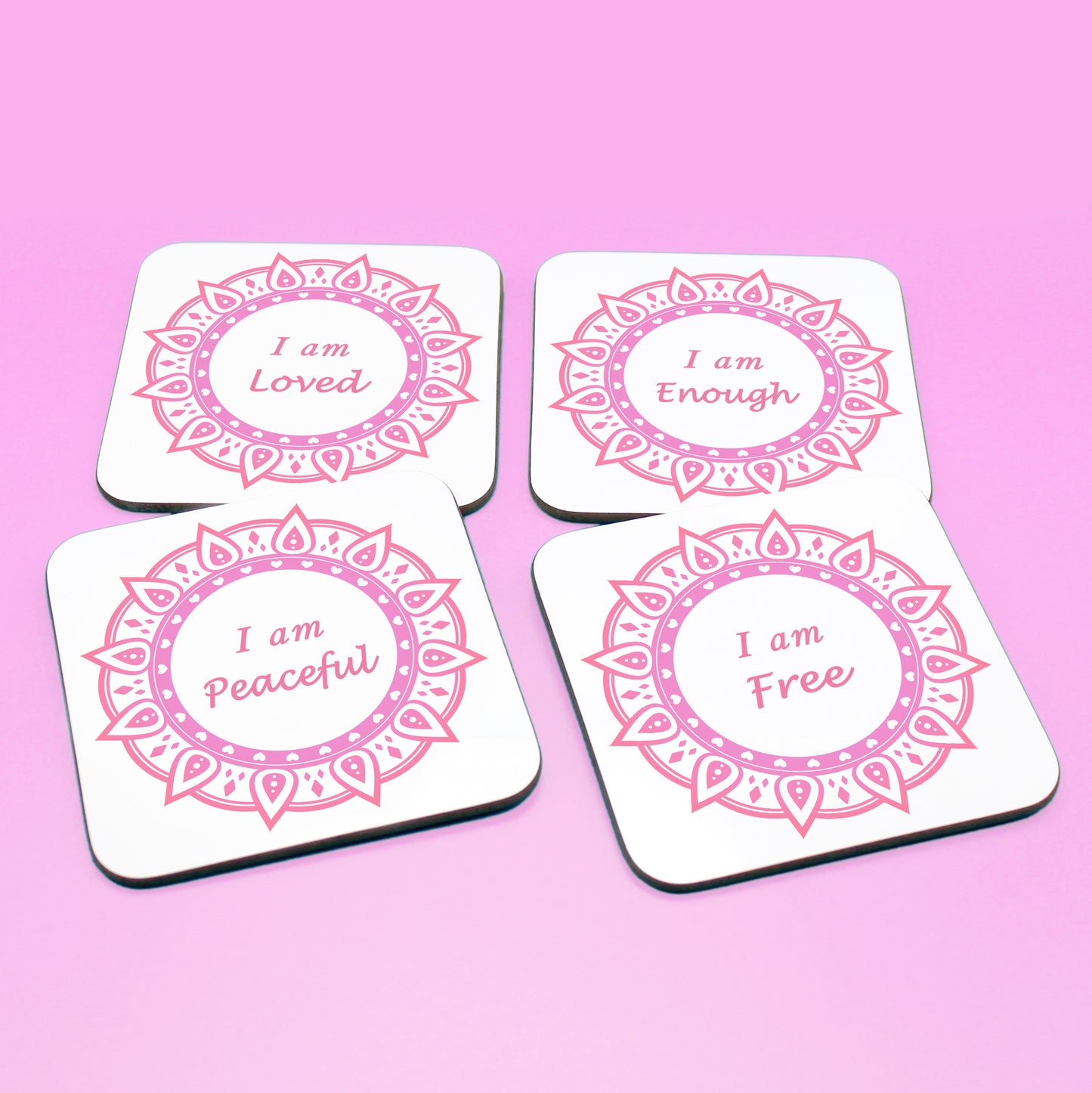 Wellbeing gift. Four square wooden backed personal affirmations coaster set. Theme is Letting Go in this set of four. Mandala design with daily affirmation wording inside the mandala.  Affirmations read I am Loved, I am Enough, I am Peaceful, I am Free (all coaster mandalas are a red and pink mandala),