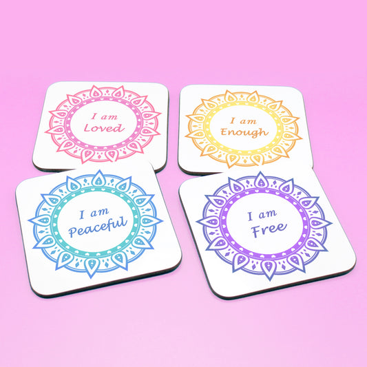 Wellbeing gift. Four square wooden backed personal affirmations coaster set. Theme is Letting Go in this set of four. Mandala design with daily affirmation wording inside the mandala.  Affirmations read I am Loved (red and pink mandala), I am Enough (yellow and orange mandala), I am Peaceful (blue mandala), I am Free (Purple mandala)