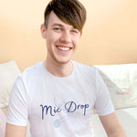 Man with brown short hair sitting wearing a Mens white short sleeve graphic tshirt with crew neck. Wording Mic Drop in navy and blue microphone outline. Music theme unisex relaxed fit slogan band tee