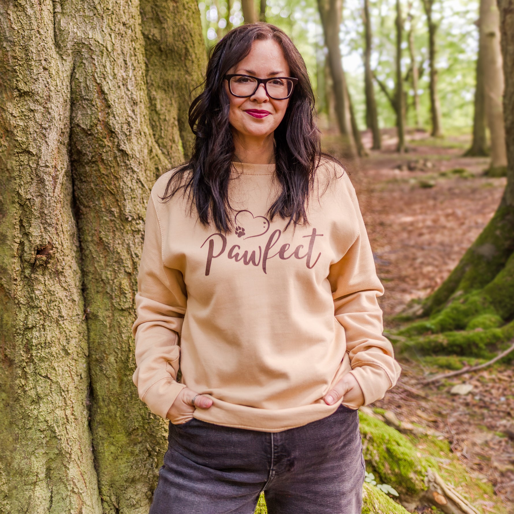 Womens Sweatshirt Dog Mom themed. Beige / Caramel colour relaxed fit long sleeve sweatshirt worn by model with black relaxed fit jeans. Slogan sweater design wording Pawfect in brown font and brown heart outline above with dog paw print within outline.