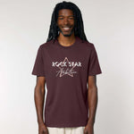 Organic Cotton Unisex relaxed fit short sleeve t shirt. Man wearing men's dark red -brown short sleeve graphic tshirt. Crew neck casual wear. Band Tee Design is pale peach star outline behind wording ROCK STAR in upper case shadowed  white text, then Ambition below in script. Rock music themed unisex top