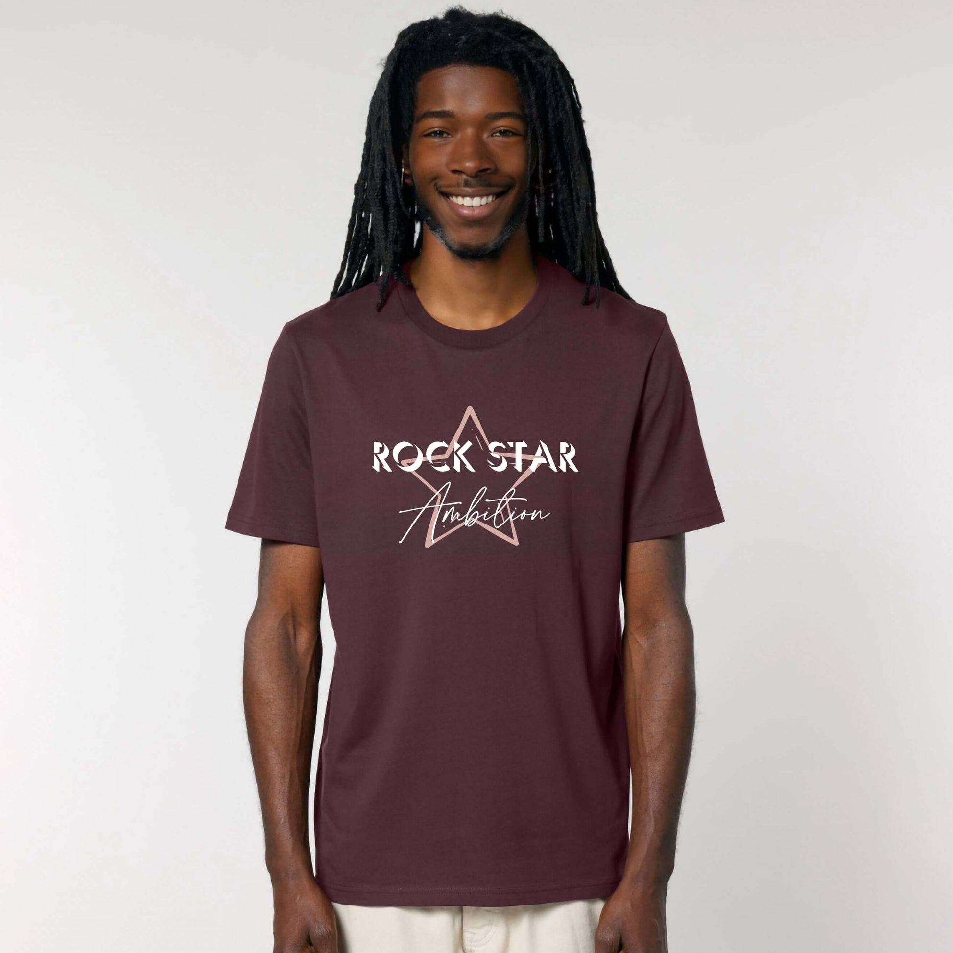 Organic Cotton Unisex relaxed fit short sleeve t shirt. Man wearing men's dark red -brown short sleeve graphic tshirt. Crew neck casual wear. Band Tee Design is pale peach star outline behind wording ROCK STAR in upper case shadowed  white text, then Ambition below in script. Rock music themed unisex top