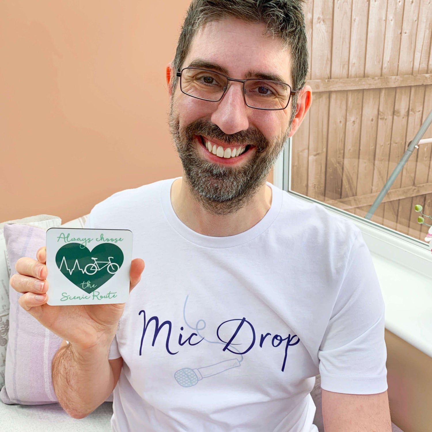 Cyclist Gift for Him. Man smiling wearing a mens white crew neck band t shirt with short sleeves. He is holding a white ceramic mug with a green design. The design is a dark green heart with a white heartbeat line shaped into mountains outline ending with