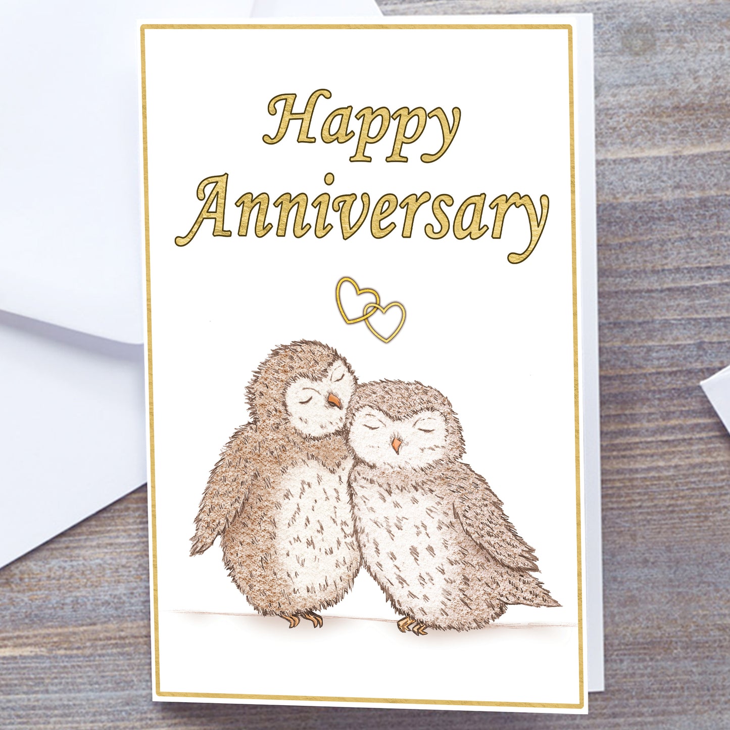 White gloss A5 Happy Anniversary Greeting card with gold text and border. Optional personalisation. Two hand-drawn fluffy brown and white owls snuggling under interlocking gold hearts. Happy Anniversary in Gold at top of card. Non-personalised option. Wedding Anniversary Card, white envelope
