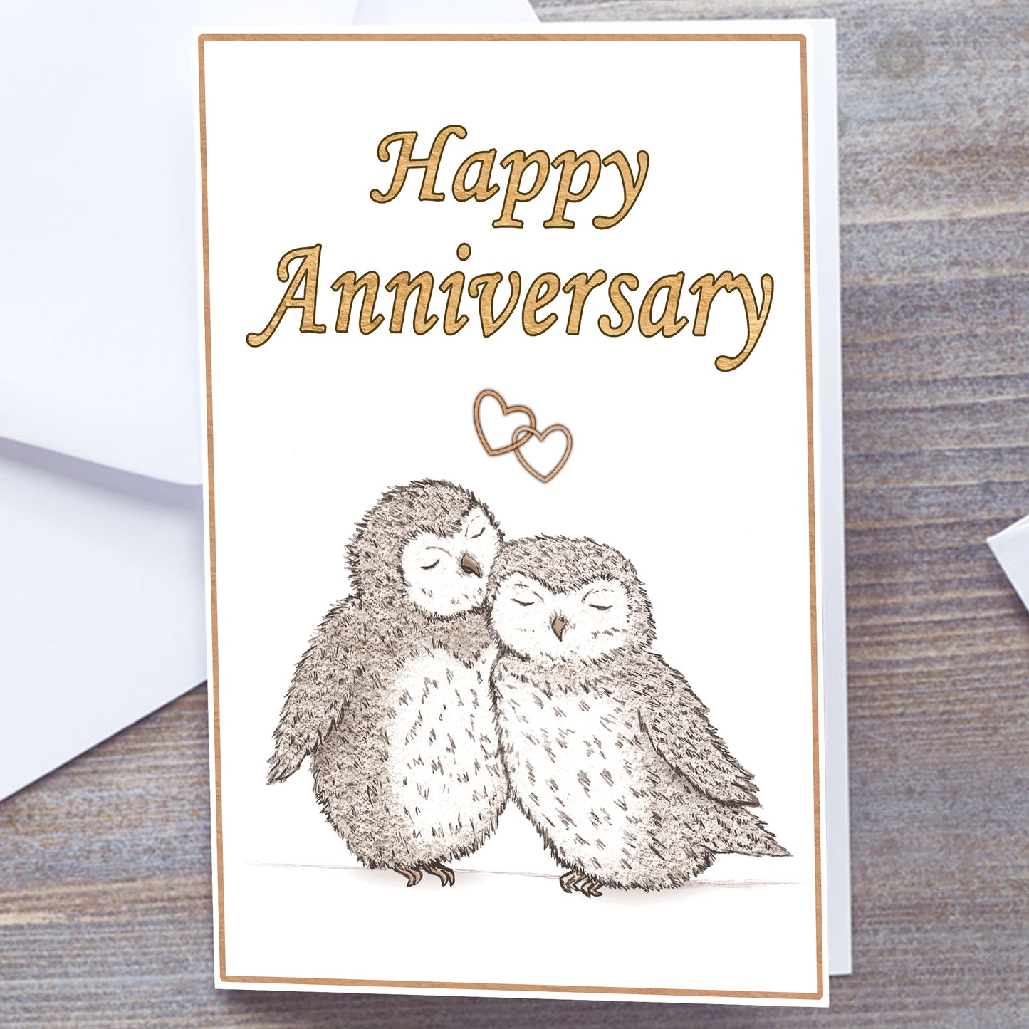 White gloss A5 Happy Anniversary Greeting card with gold text and border. Optional personalisation. Two hand-drawn fluffy grey/brown owls snuggling under interlocking gold hearts. Happy Anniversary in Gold at the top of card. Non-personalised version. Gold Wedding Anniversary Card, white envelope