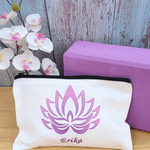 Gift for yoga lovers. Small personalised yoga theme make up bag. White with black zipped opening. Purple lotus flower design and name in purple below. White orchid and purple yoga block in background