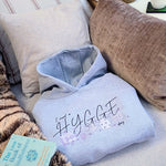 Hygge inspiration. Oversized grey womens hoodie with slogan I need a hygge day. Hygge home with book and fleece.